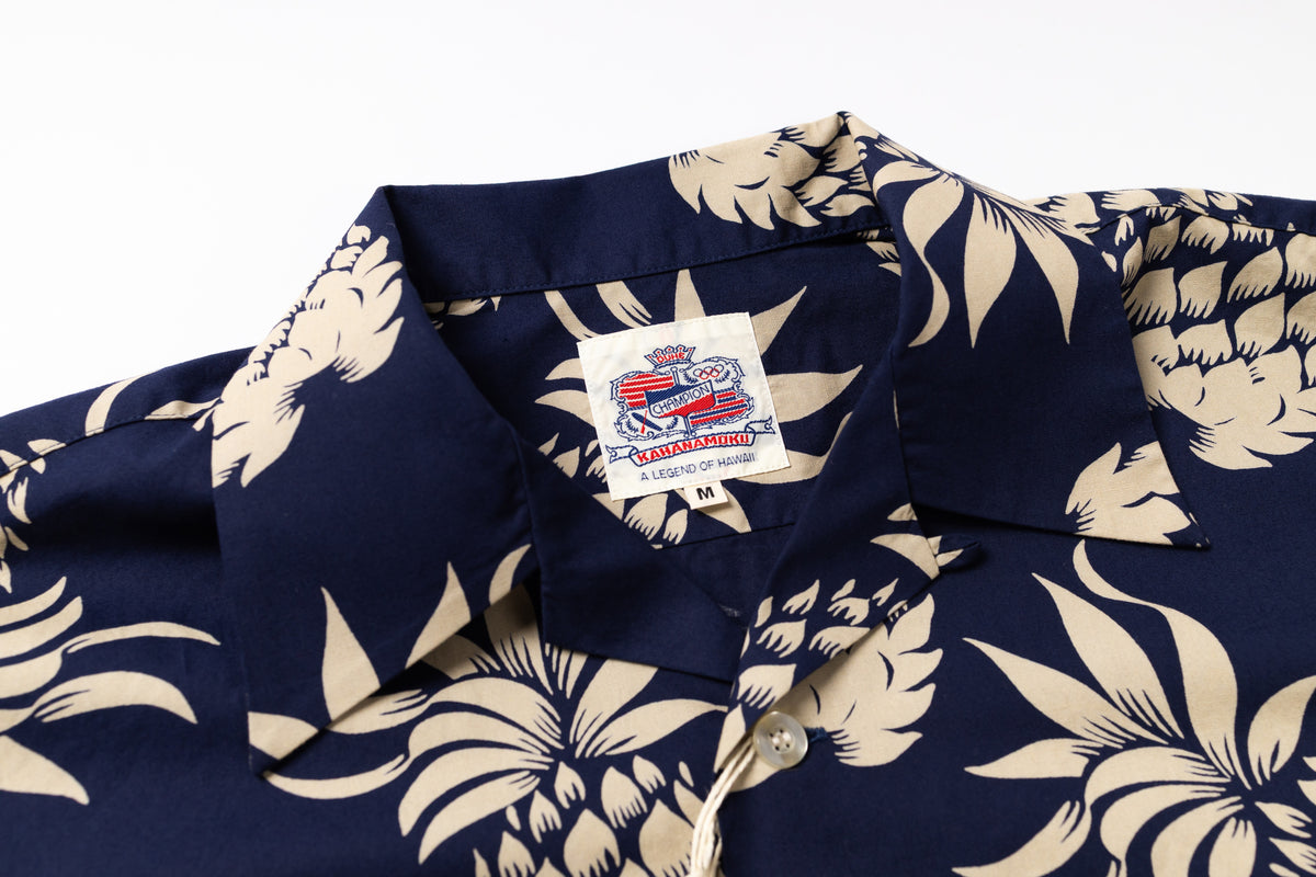 Close-up of a navy blue short-sleeve button-up shirt with a beige tropical floral print, featuring a visible brand label on the collar.