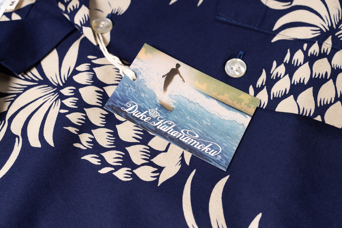 Close-up of a navy blue short-sleeve button-up shirt with a white tropical floral print, featuring a hangtag 
