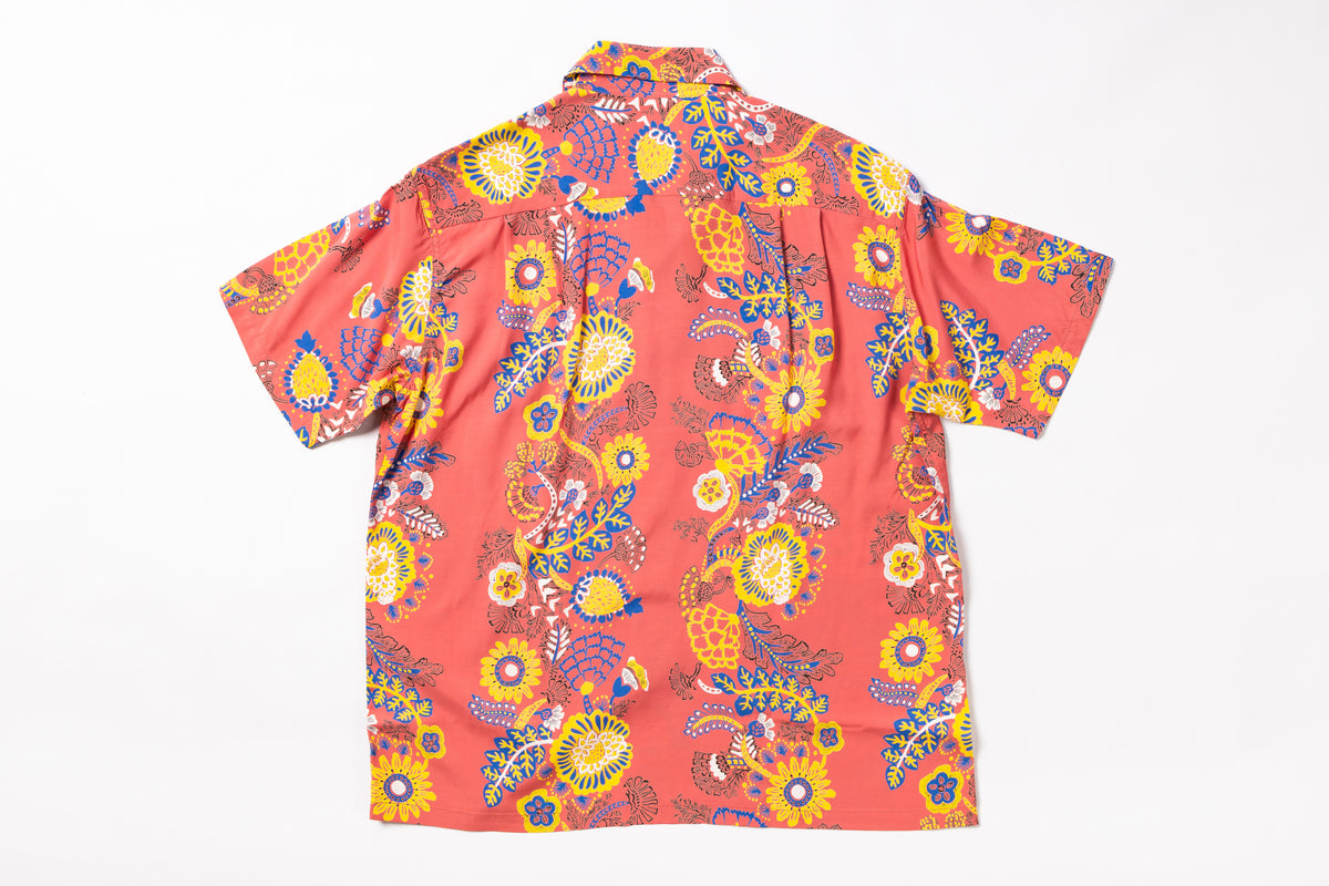 A short-sleeve button-up shirt with a vibrant retro paisley and floral pattern in orange, yellow, blue, and white, laid flat against a white background.