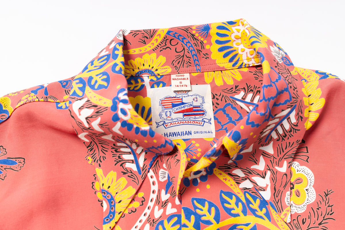 Close-up of a Hawaiian shirt collar showing a colorful floral and paisley print in coral pink, yellow, blue, and white, with a visible 'Hawaiian Original' neck label.