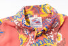 Close-up of a Hawaiian shirt collar showing a colorful floral and paisley print in coral pink, yellow, blue, and white, with a visible 'Hawaiian Original' neck label.