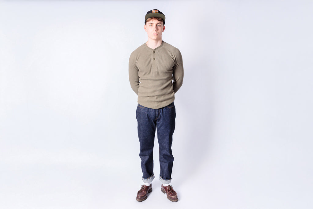 Person wearing a green shirt, blue jeans, and a cap on a white background