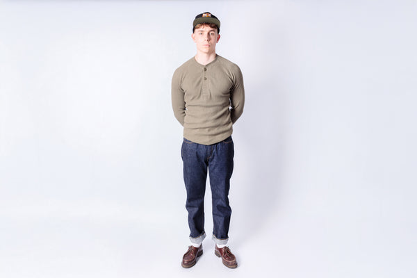 Person wearing a green shirt, blue jeans, and a cap on a white background