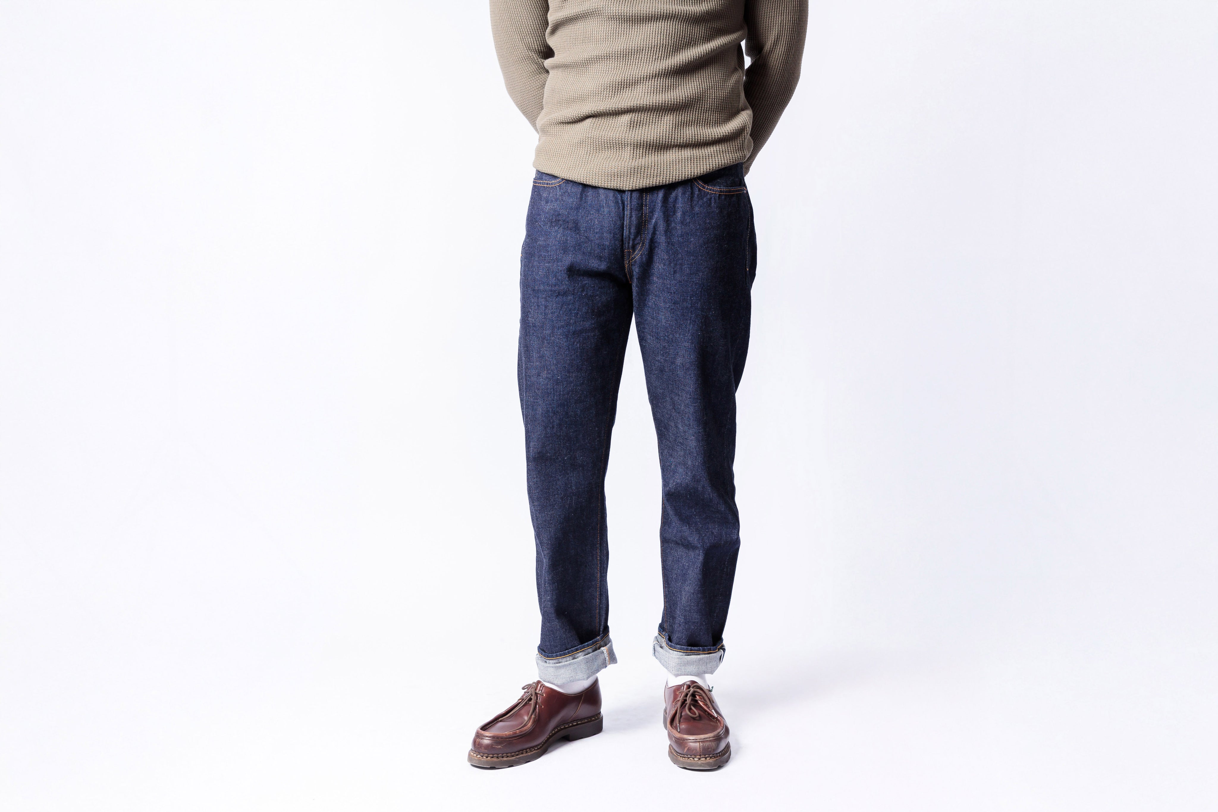 Person wearing blue jeans and a beige sweater on a white background