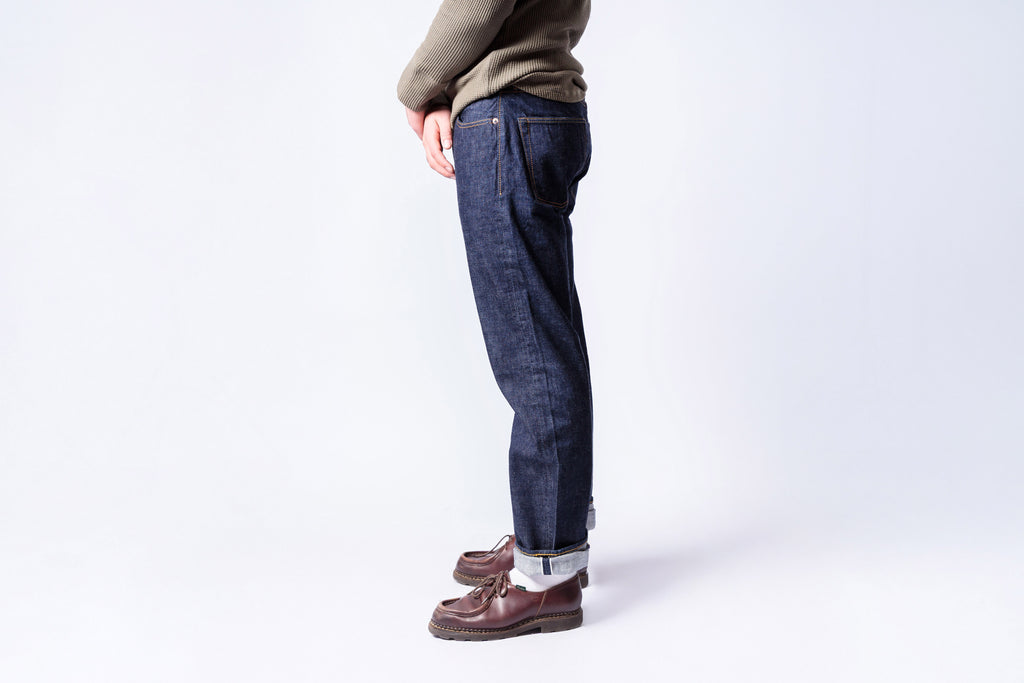 Person wearing dark blue jeans and brown shoes on a white background