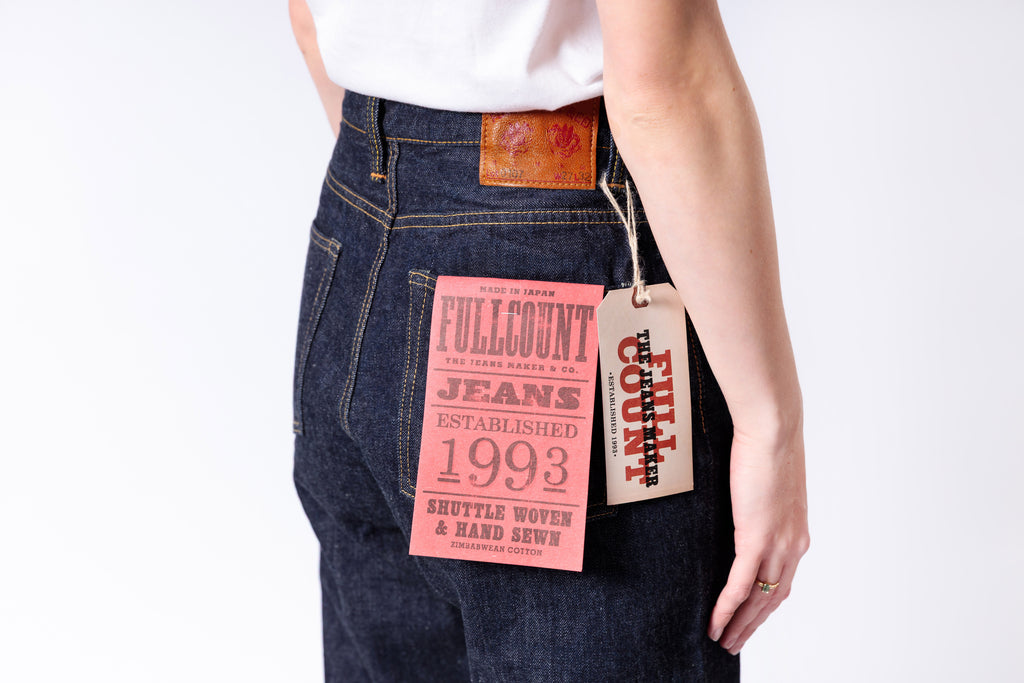 Person wearing dark blue jeans with Fullcount Jeans tags on a white background