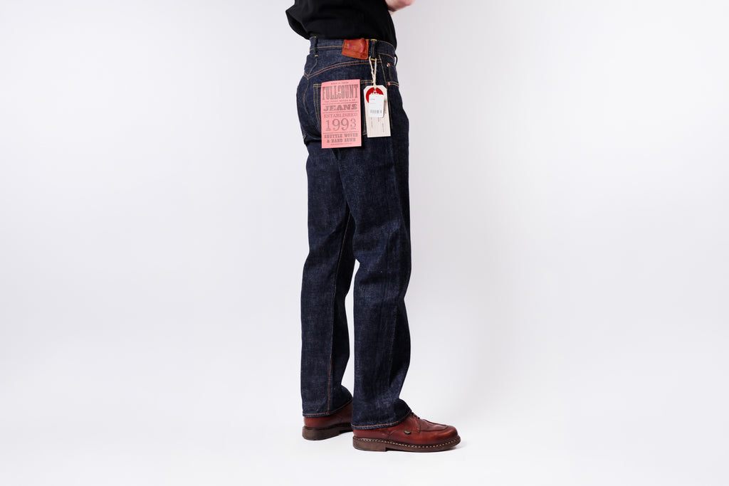 Person wearing dark blue jeans with tags on a white background