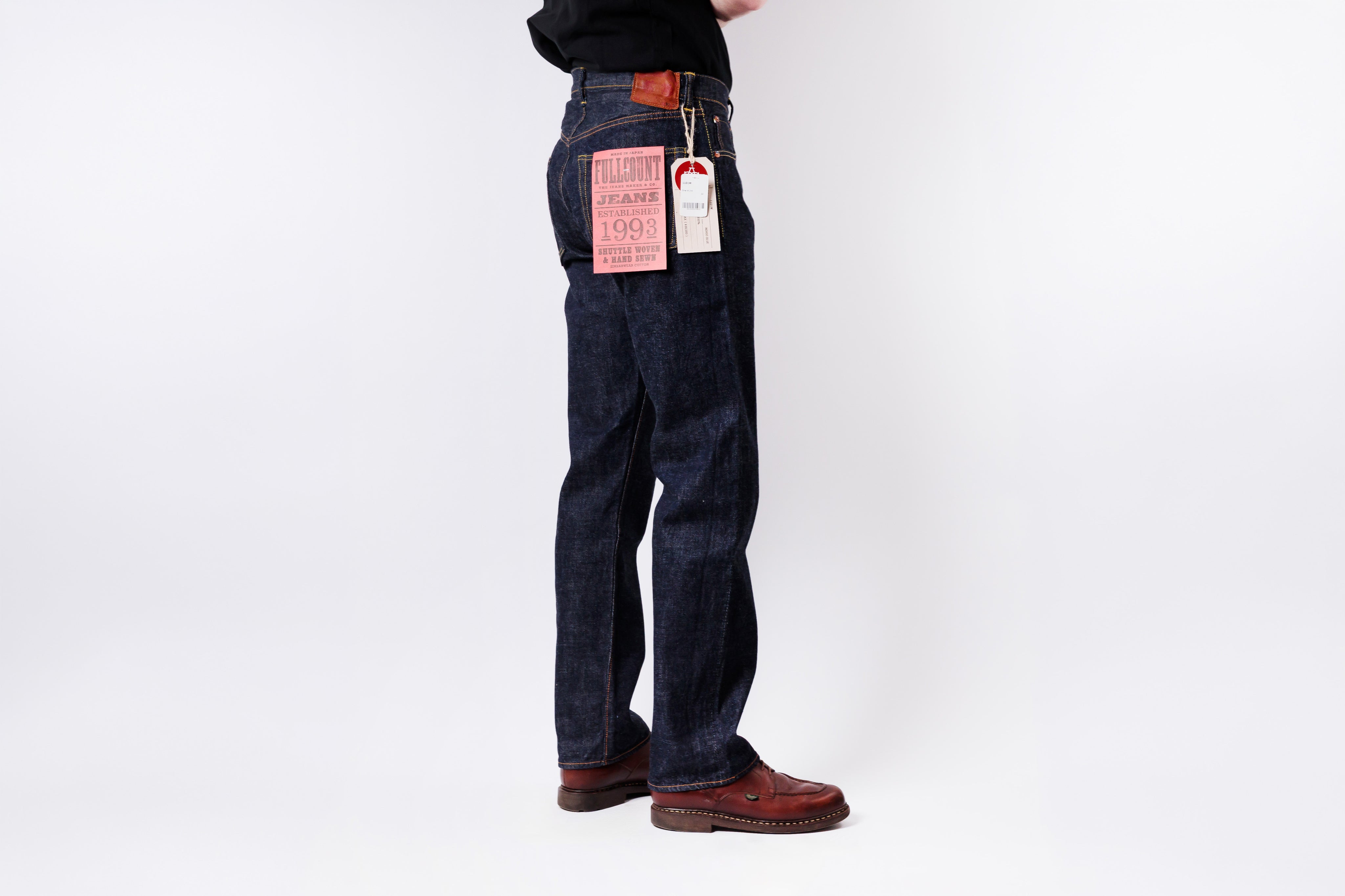 Person wearing dark blue jeans with tags on a white background