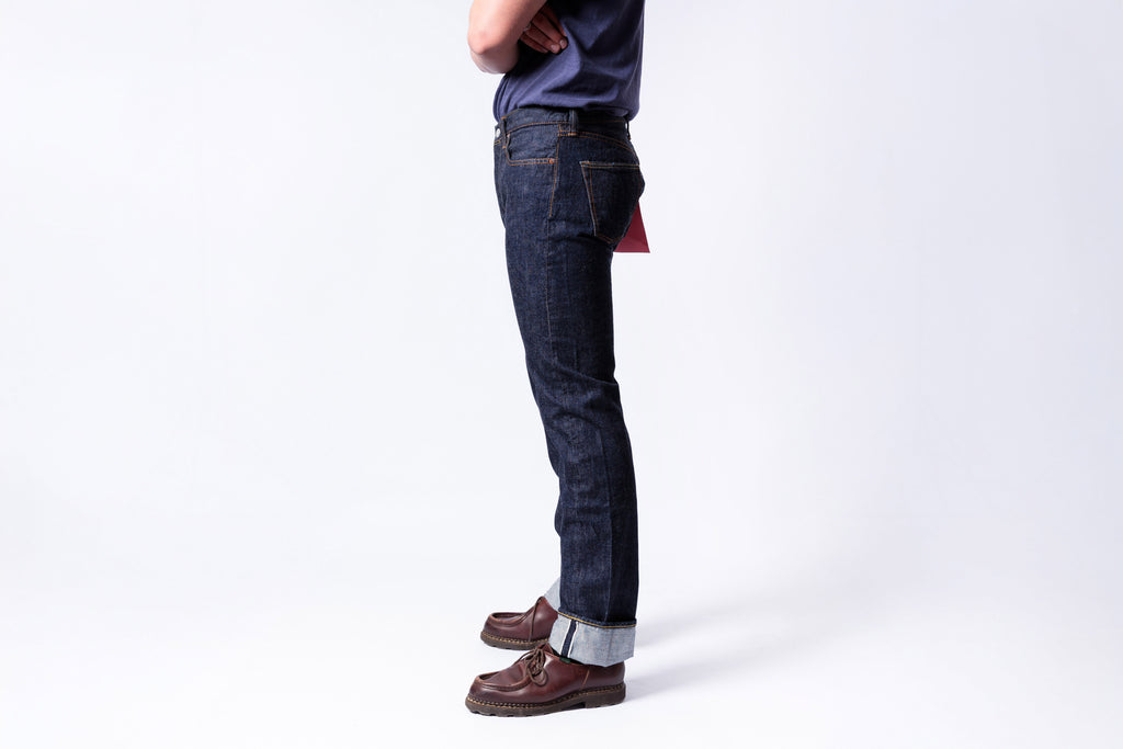 Person wearing dark blue jeans and brown shoes on a white background