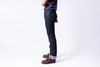 Person wearing dark blue jeans and brown shoes on a white background