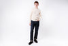 Man wearing a beige sweater and dark jeans on a white background