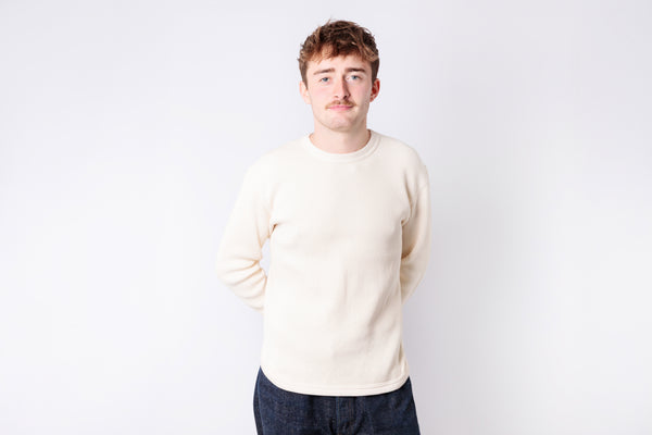 Man wearing a cream sweater and dark pants against a white background