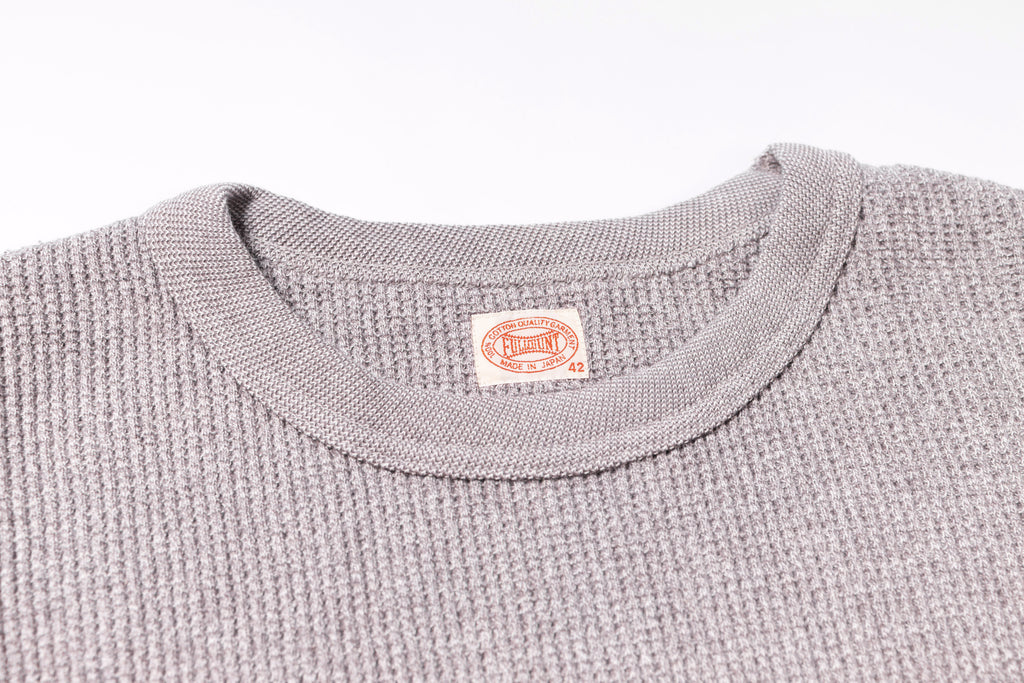 Close-up of a textured gray sweater with a brand label on a white background