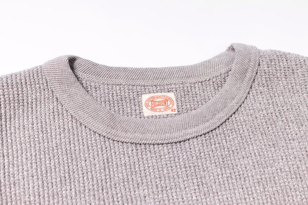 Close-up of a textured gray sweater with a brand label on a white background