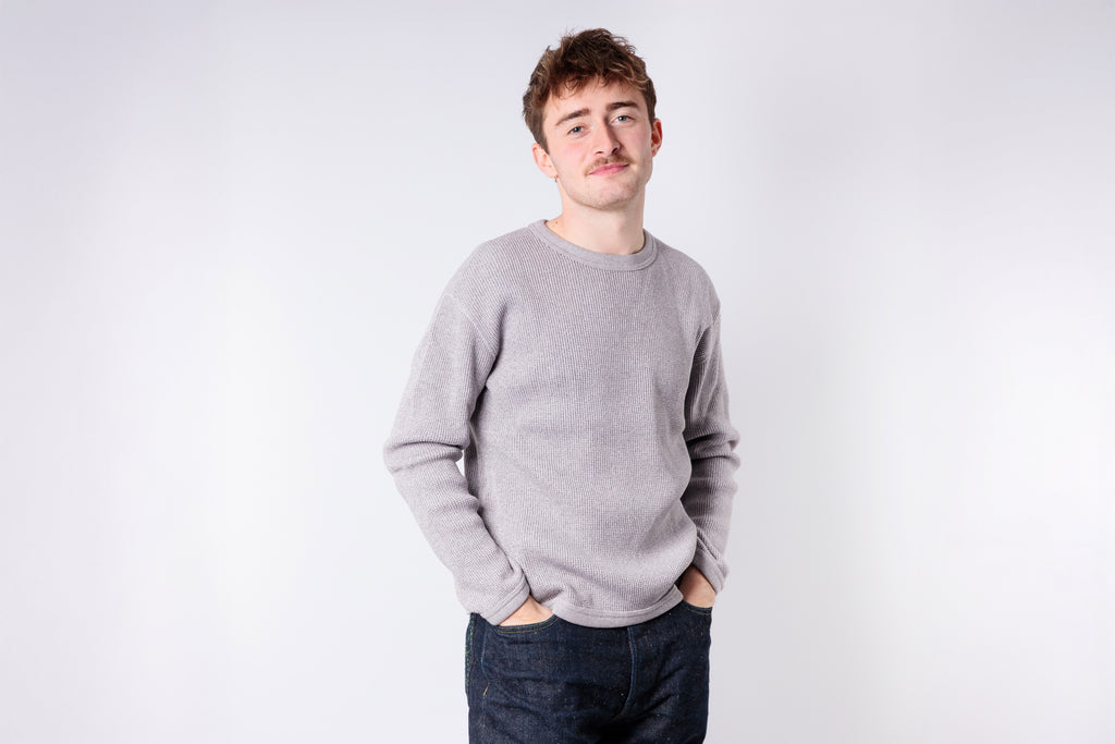 Man wearing a gray sweater and dark jeans against a white background