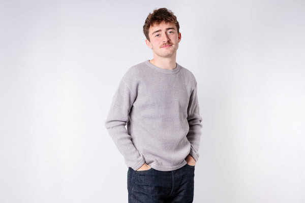 Man wearing a gray sweater and dark jeans against a white background