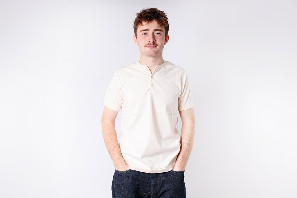 Man wearing a light-colored polo shirt and dark pants against a white background