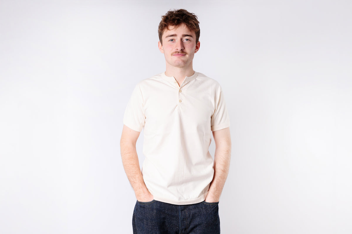 Man wearing a light-colored polo shirt and dark pants against a white background