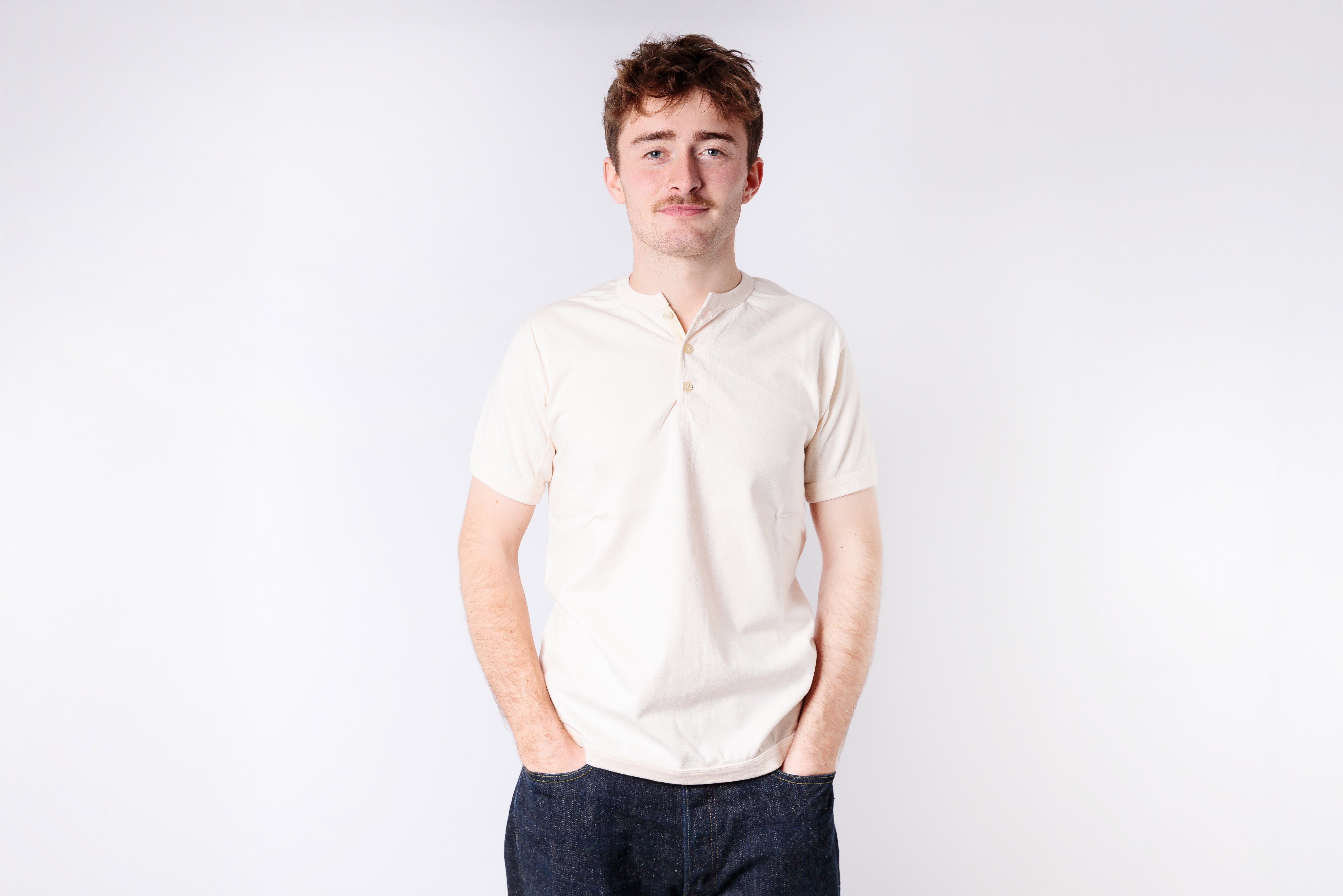 Man wearing a light-colored polo shirt and dark pants against a white background