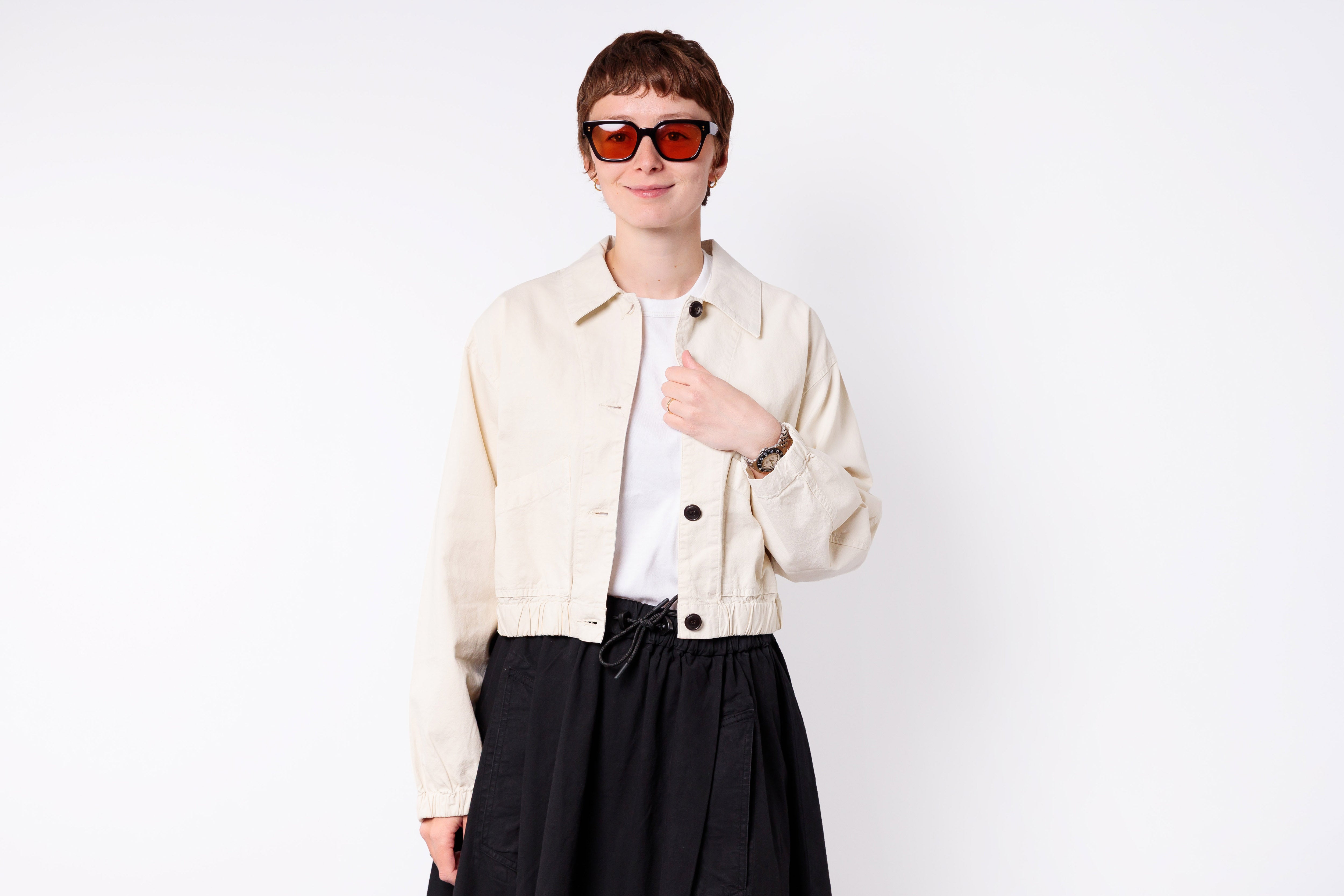 Person wearing a beige jacket and black skirt on a white background