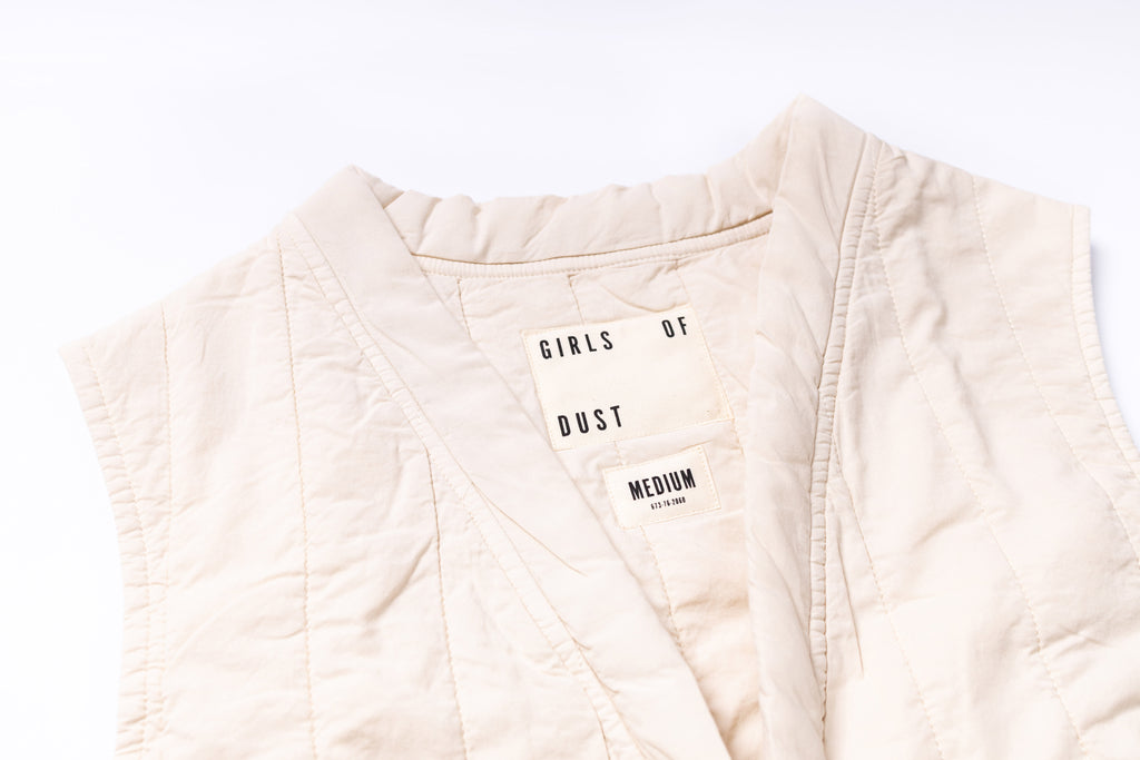 Beige quilted jacket with 'GIRLS OF DUST' text on a white background