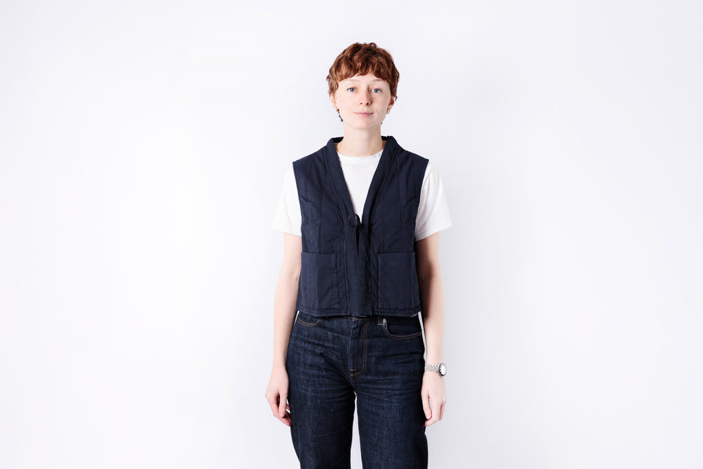 Person wearing a navy vest and dark jeans on a white background