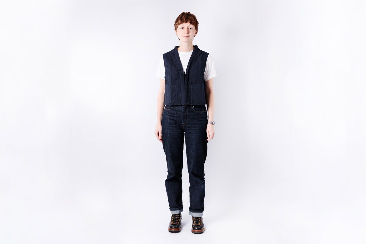 Person wearing a dark vest and jeans on a white background