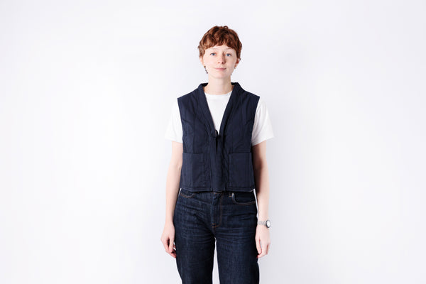 Person wearing a navy vest and dark jeans on a white background