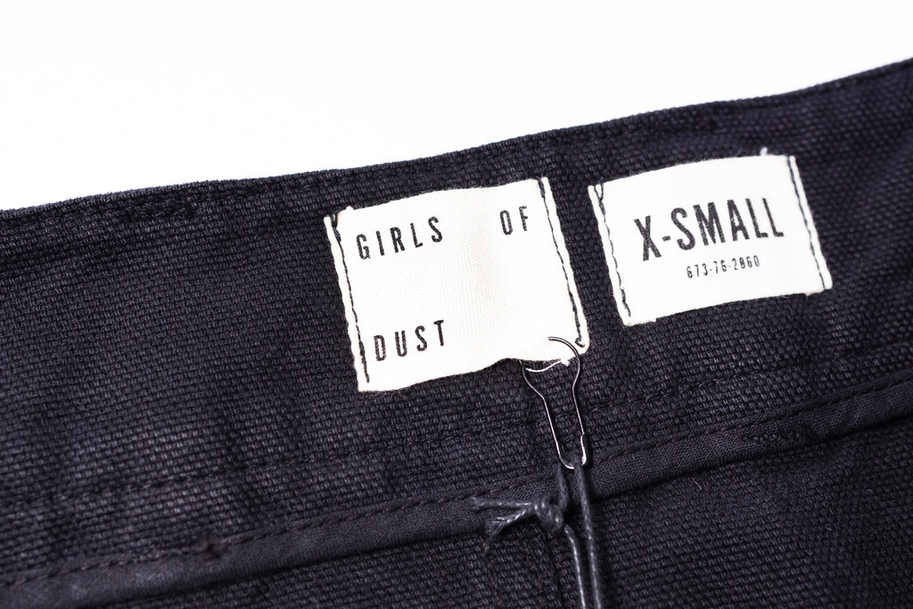Close-up of black pants with 'GIRLS OF DUST' and 'X-Small' labels.