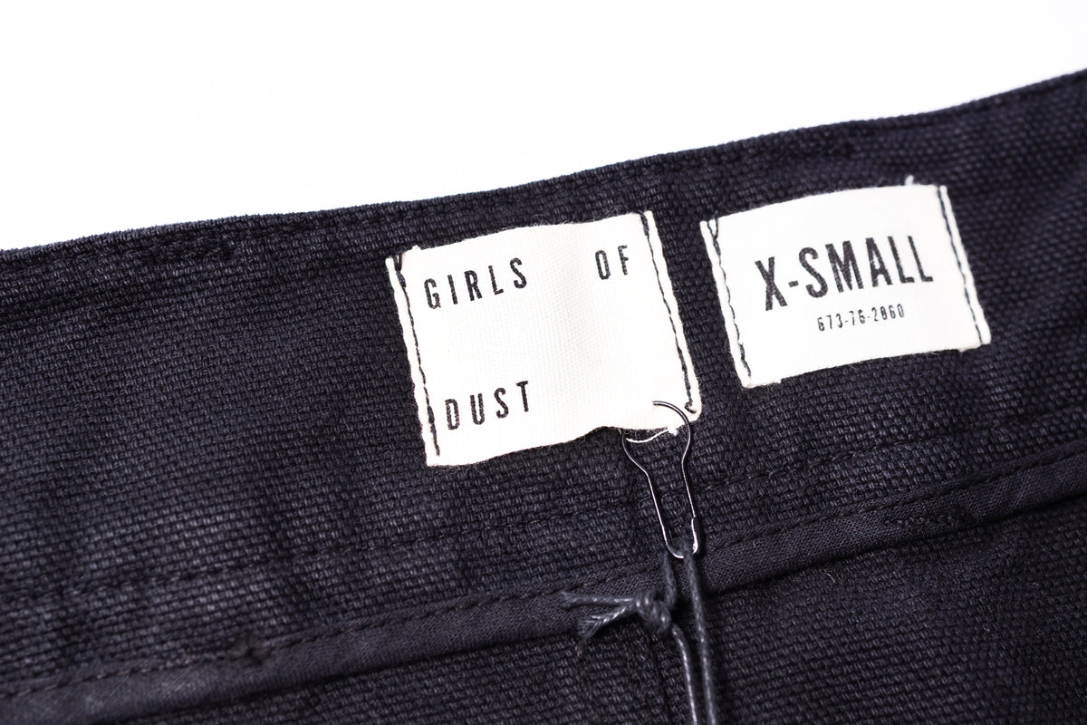 Close-up of black pants with 'GIRLS OF DUST' and 'X-Small' labels.