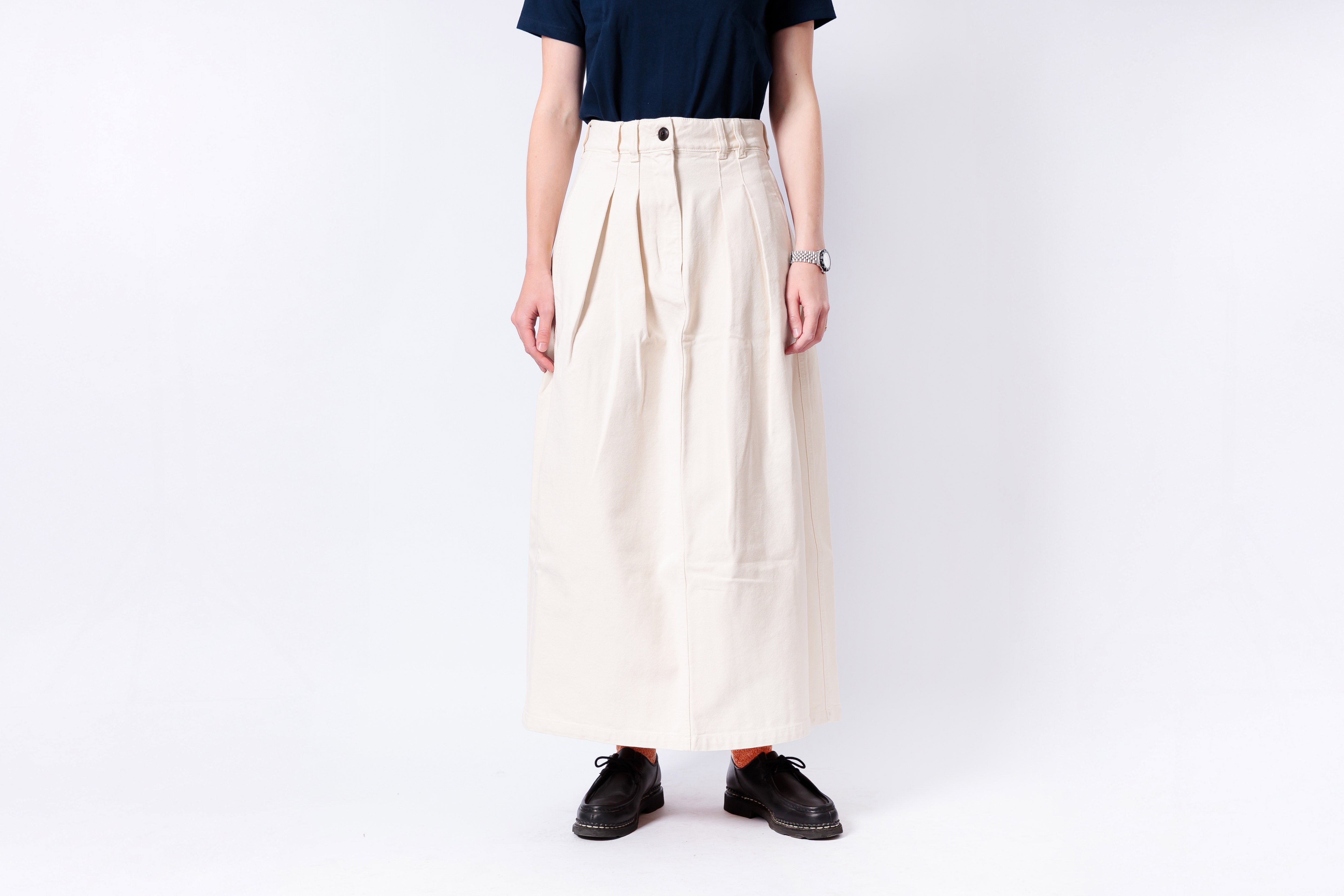 Person wearing a long beige skirt with a plain background
