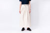 Person wearing a long beige skirt with a plain background