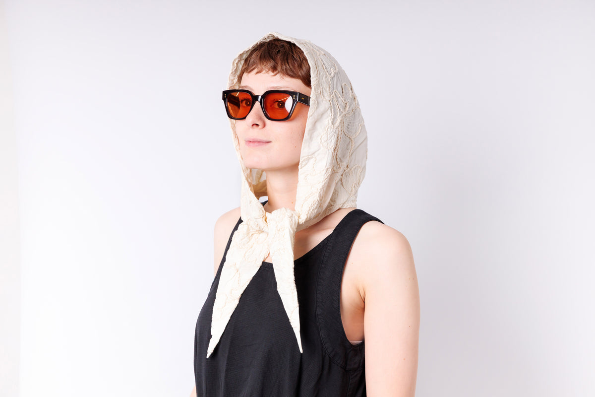 Woman wearing a white headscarf and red sunglasses on a light gray background