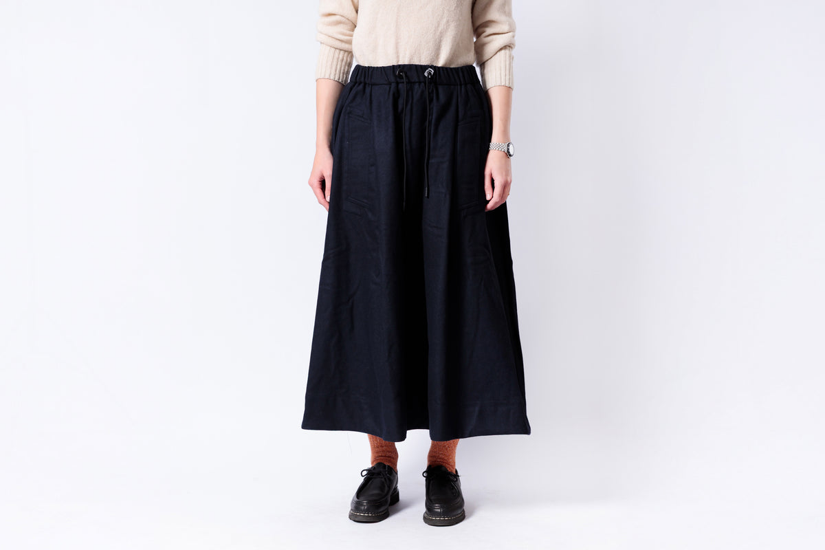Person wearing a black skirt and beige sweater on a white background