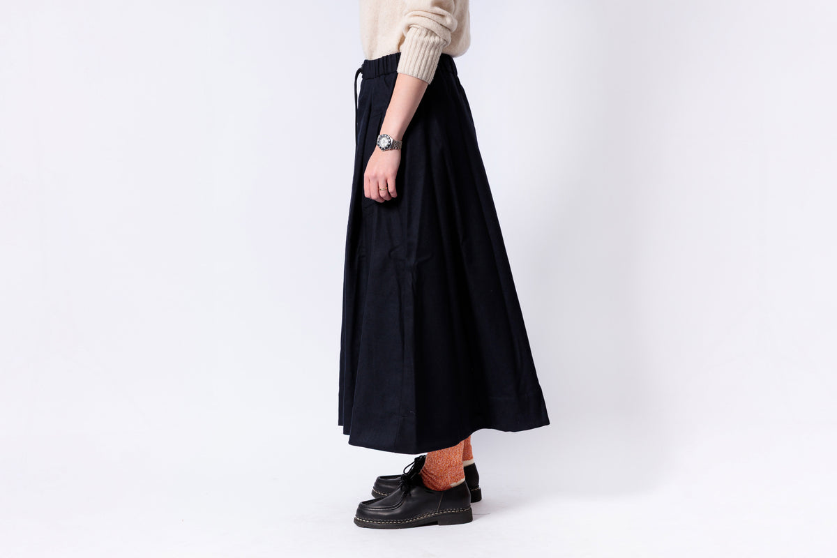 Person wearing a black skirt and beige sweater on a white background