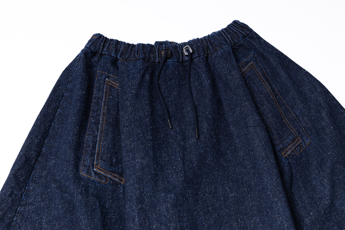 Close-up of dark indigo denim pants showing the elastic waistband, drawstring, and side pocket details on a white background.
