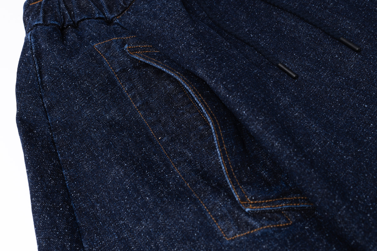 Close-up of dark indigo denim fabric showing a side pocket with contrasting tan stitching and a drawstring detail.
