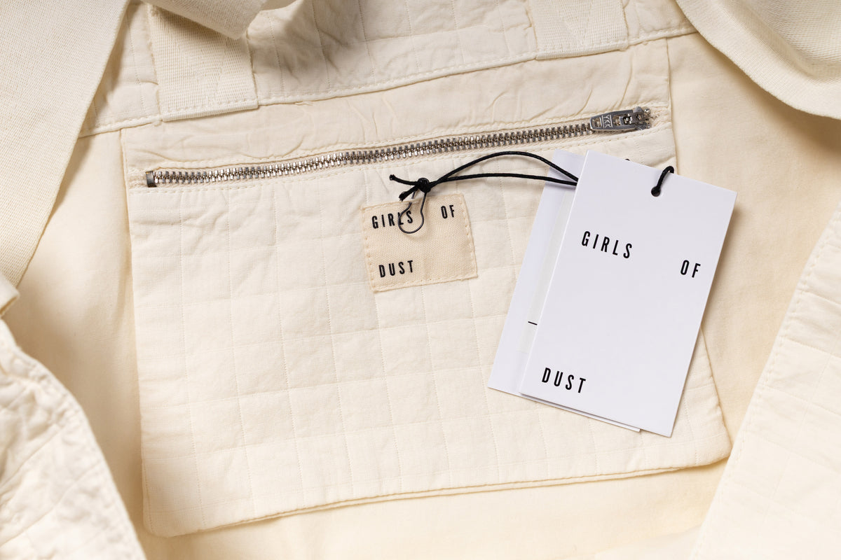Close-up of a beige jacket with 'Girls of Dust' tags attached.