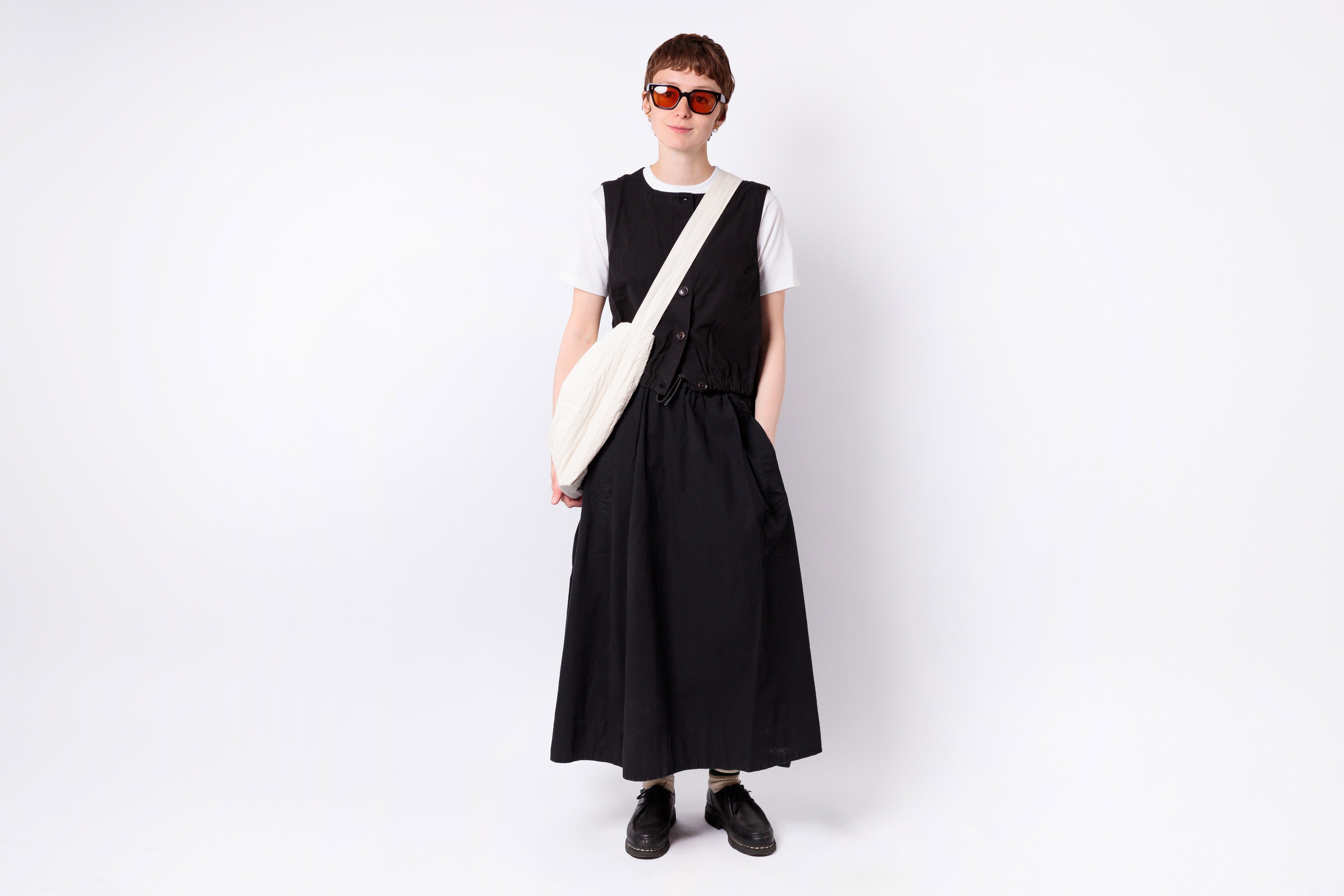 Person wearing a black dress and sunglasses holding a white bag on a white background