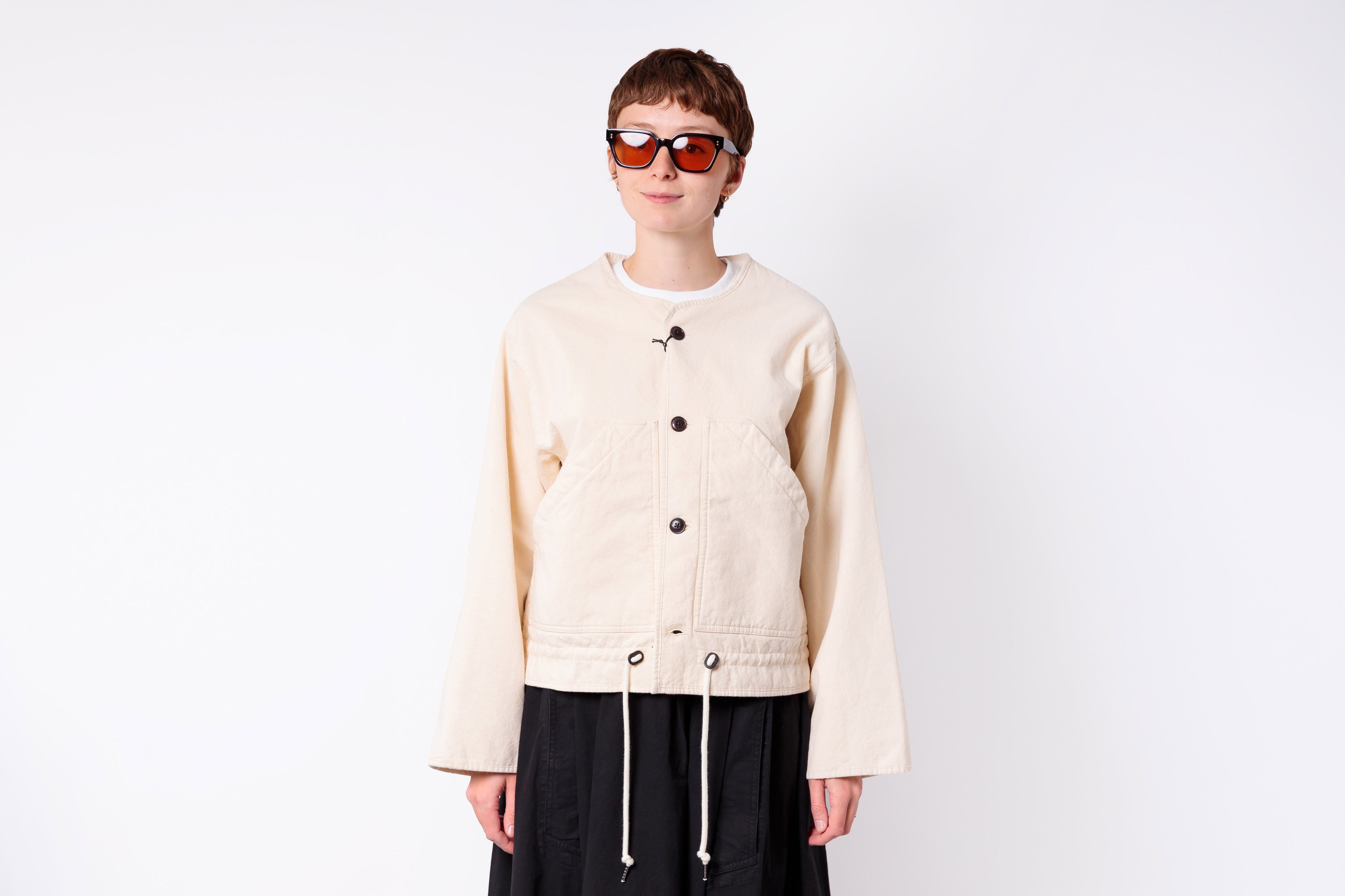 Person wearing a beige jacket and sunglasses on a white background
