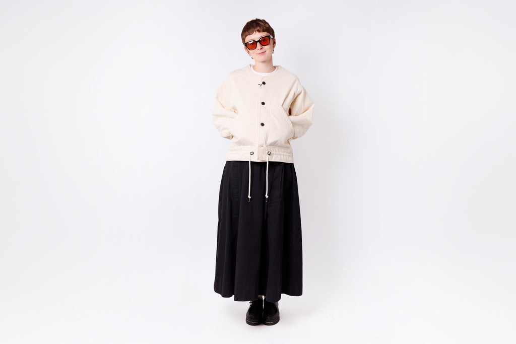 Person wearing a beige cardigan, black skirt, and sunglasses on a white background