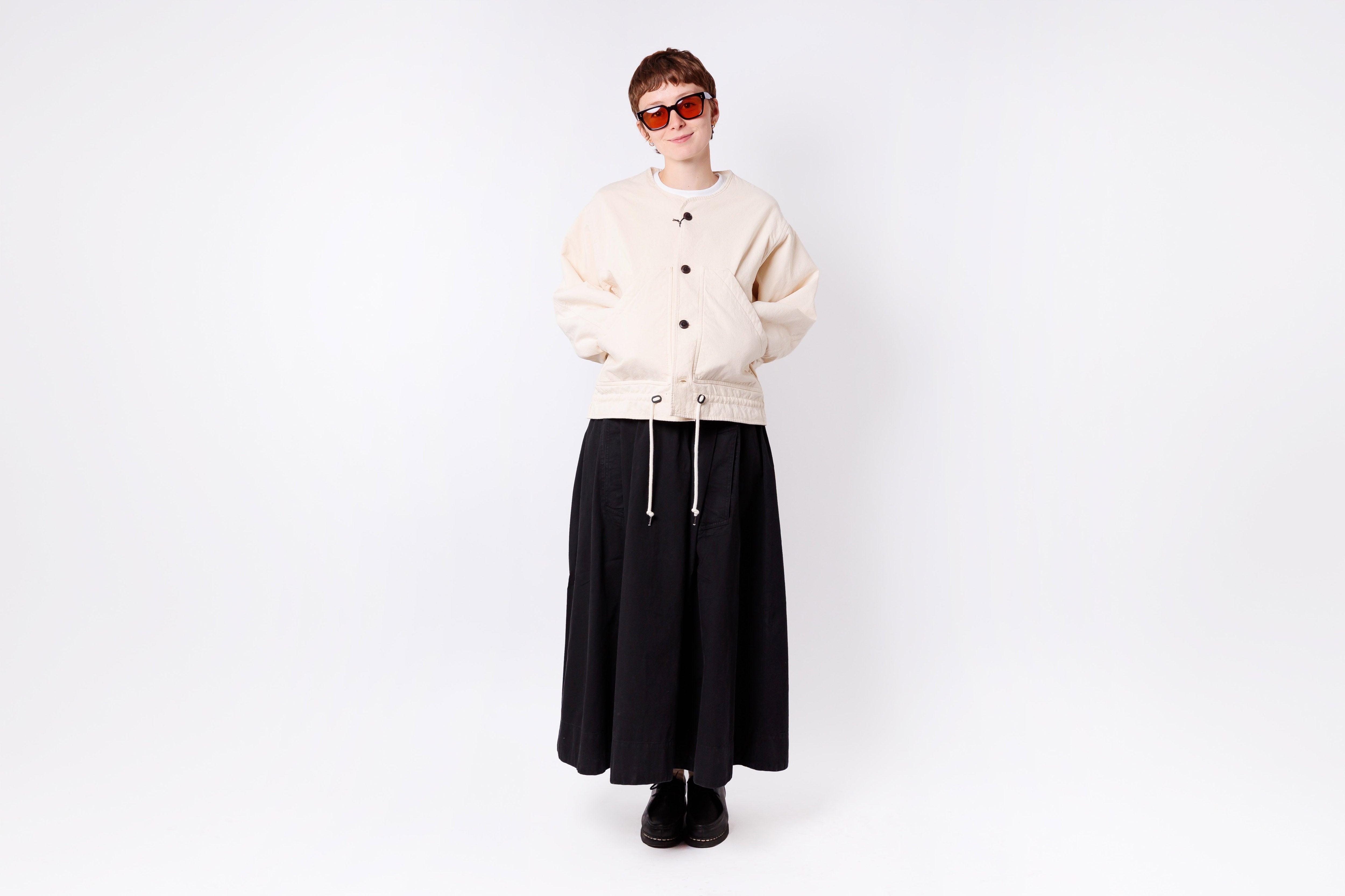 Person wearing a beige cardigan, black skirt, and sunglasses on a white background