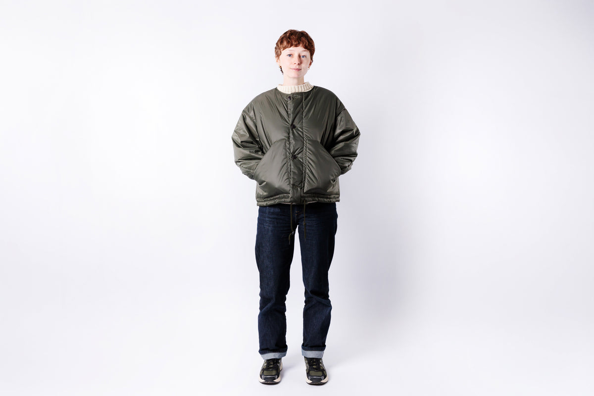 Person wearing a green jacket and dark jeans on a white background