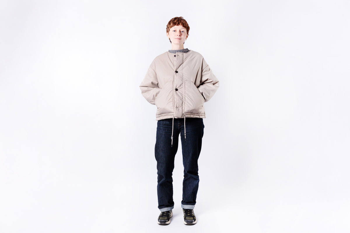 Person wearing a beige cardigan and dark jeans on a white background