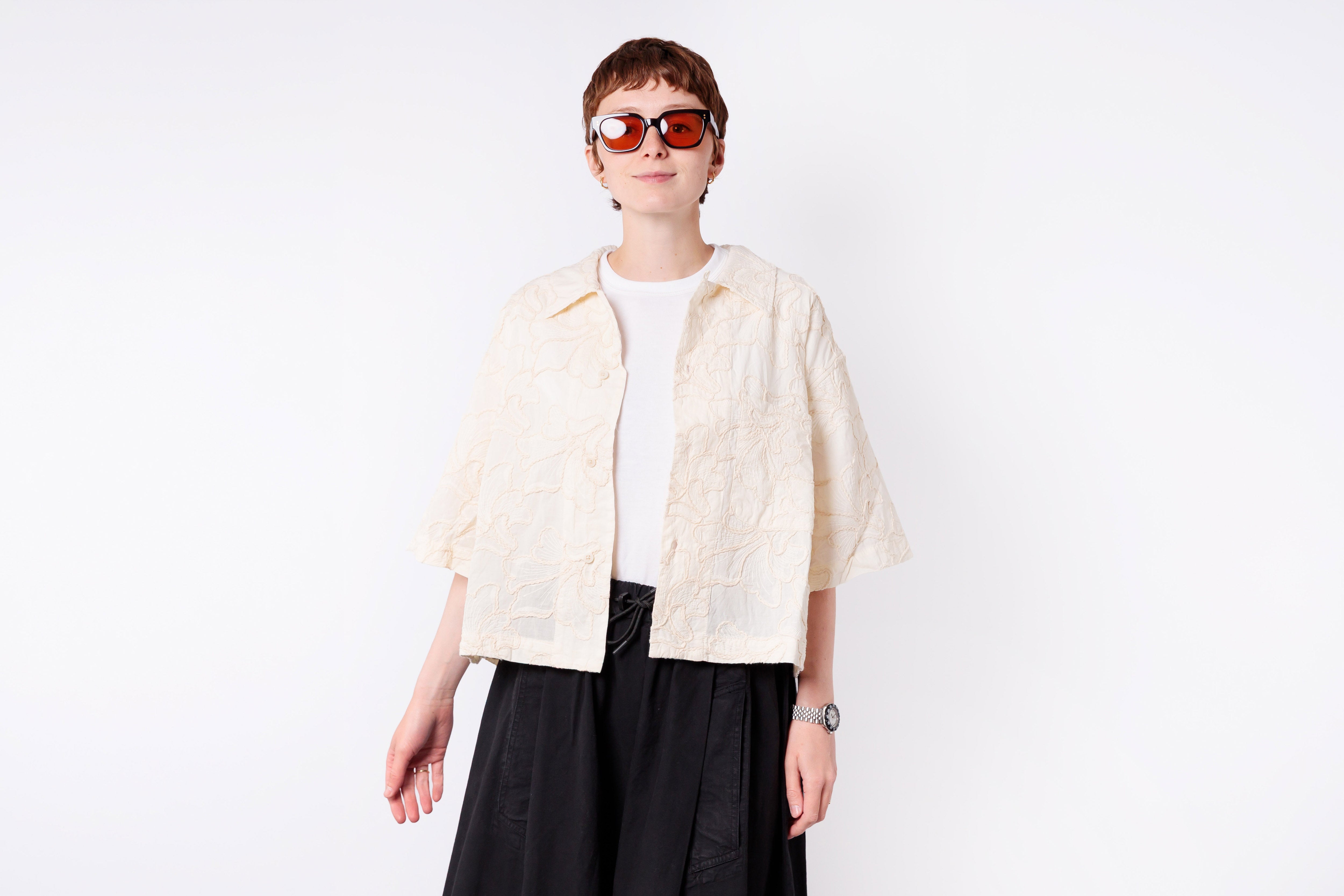 Person wearing a cream jacket over a white shirt with black pants on a white background