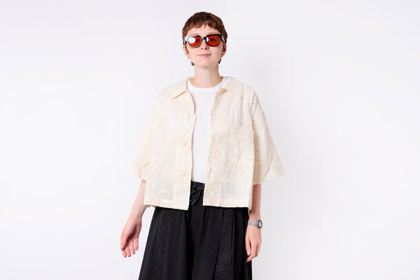Person wearing a cream jacket over a white shirt with black pants on a white background