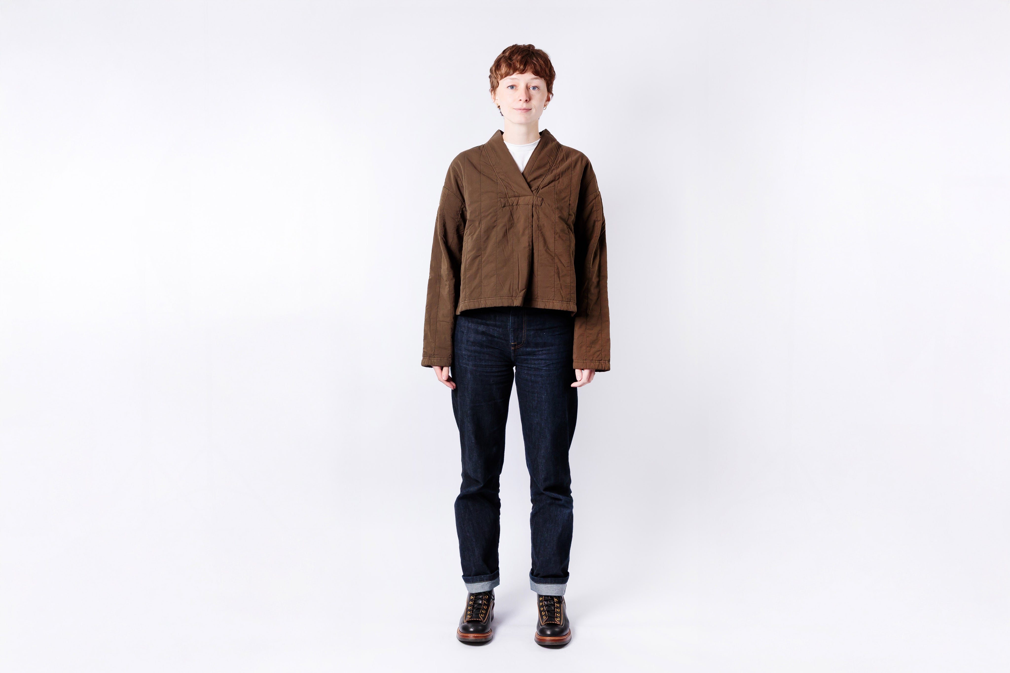 Person wearing a brown jacket and dark jeans on a white background