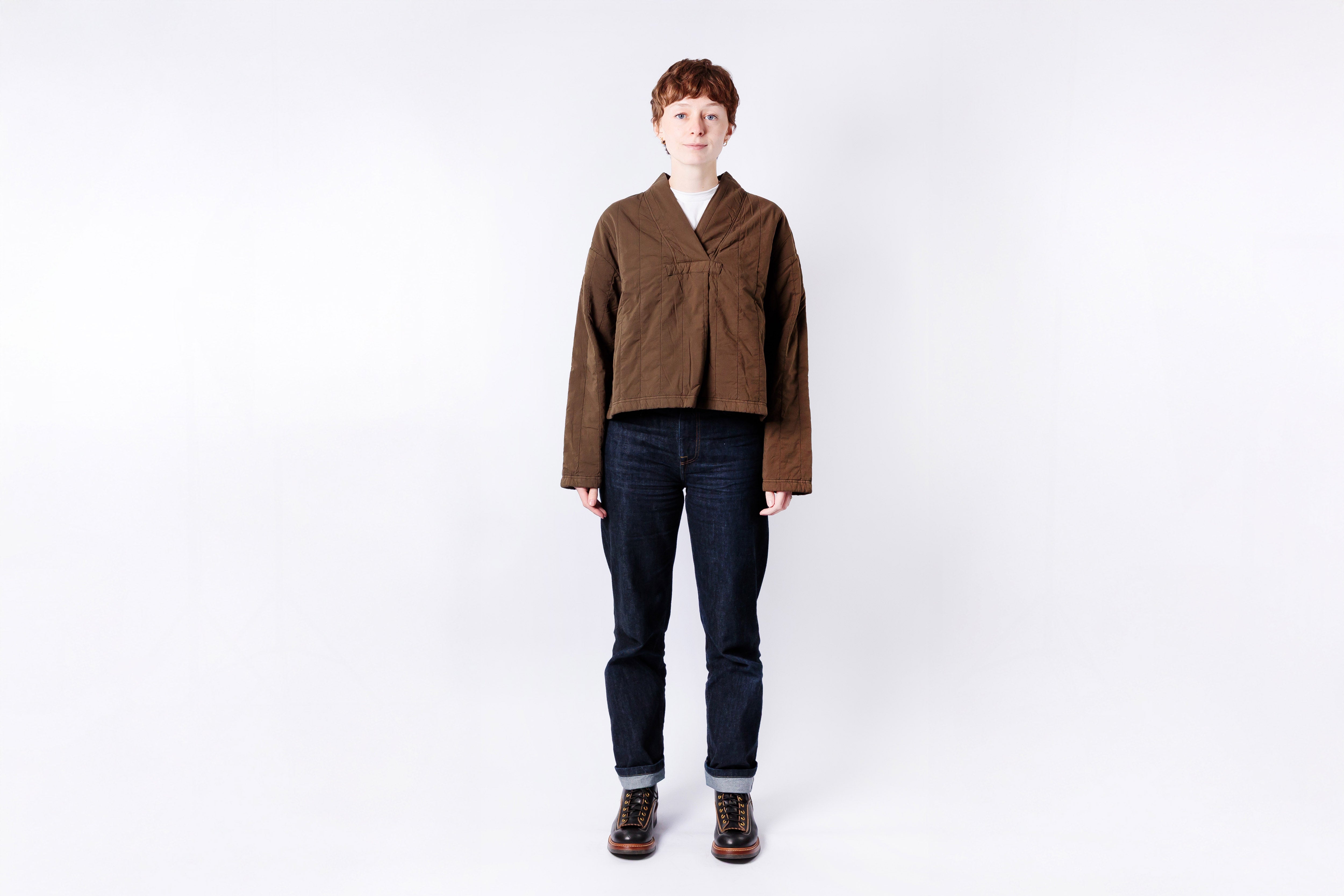 Person wearing a brown jacket and dark jeans on a white background