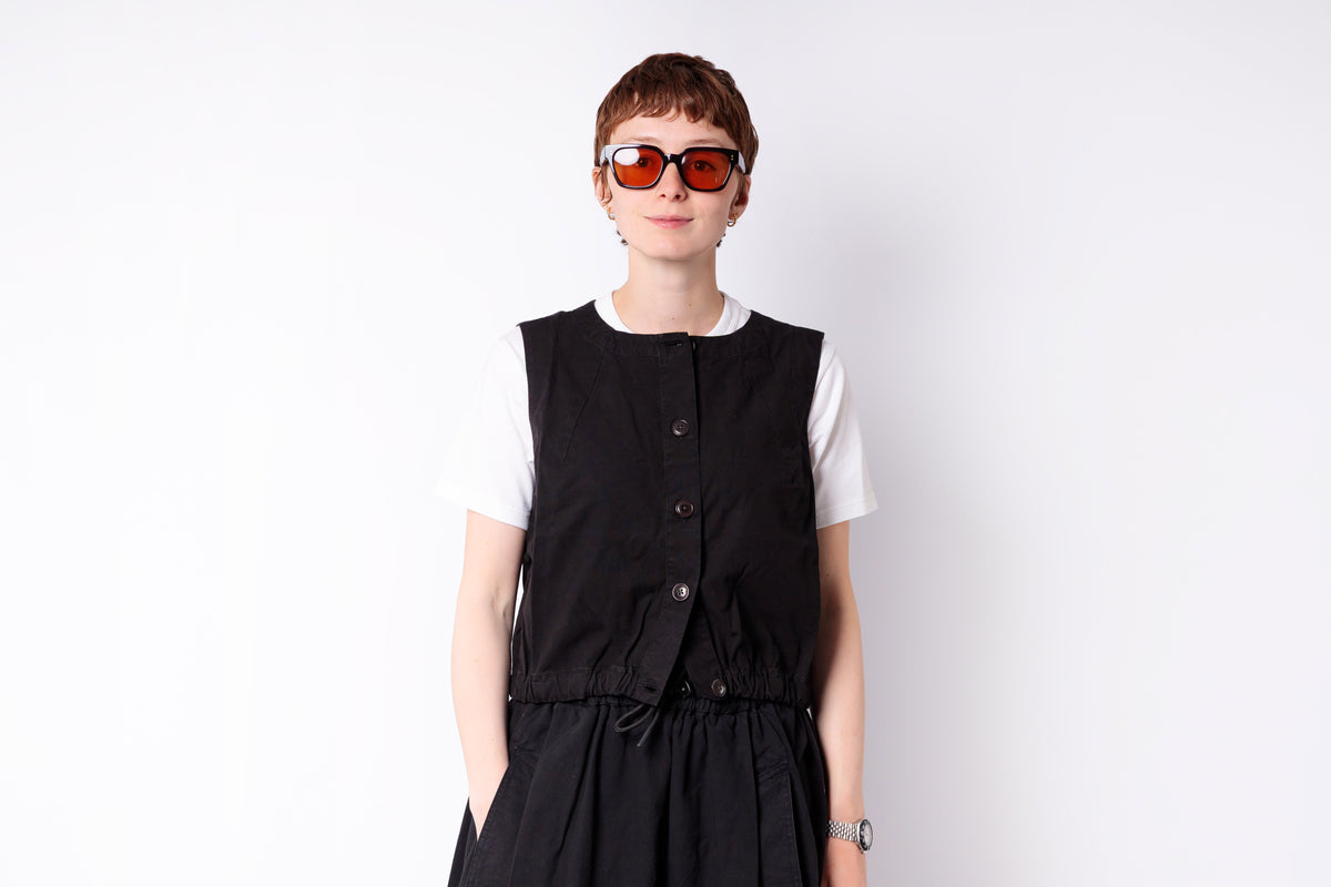 Person wearing a black vest over a white shirt on a white background
