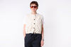 Person wearing a cream vest over a white shirt with dark pants on a white background